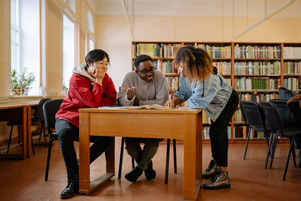Scholarships Diverse group of students studying together at a library table, fostering teamwork and learning.