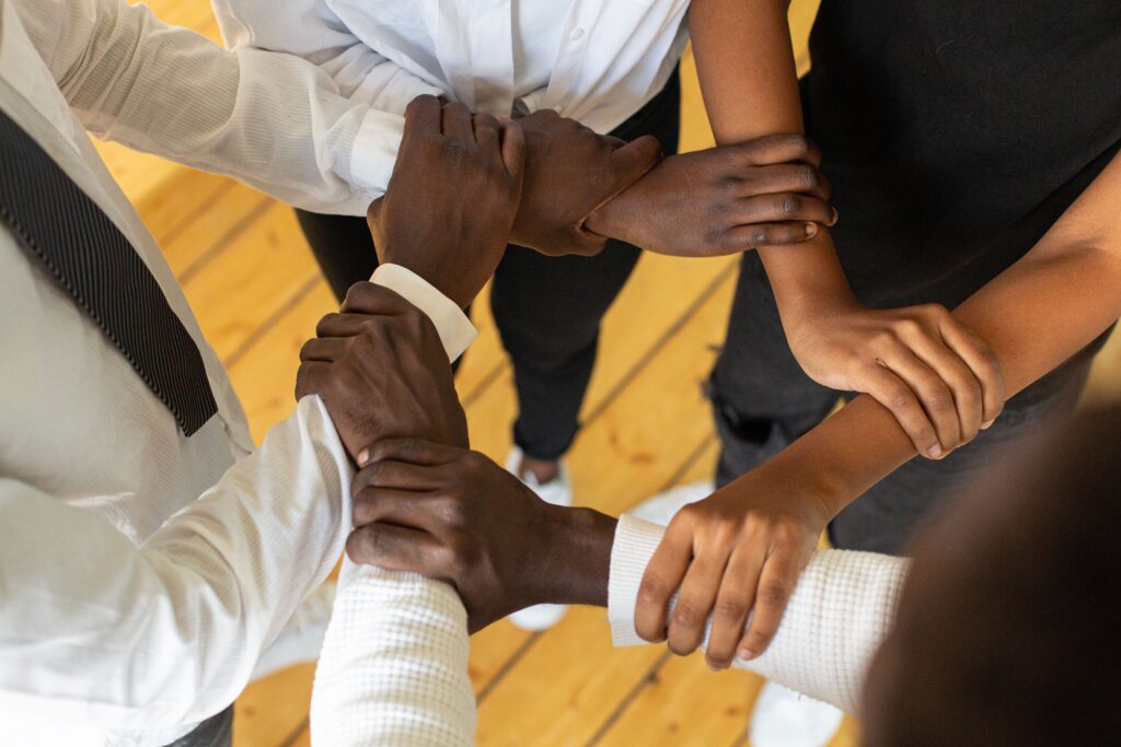 What We Do Close-up of diverse hands in a circle, symbolizing teamwork and unity.
